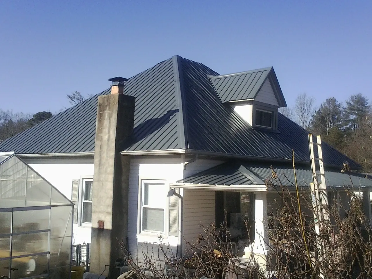 Dark blue standing seam metal roof on a white farmhouse with dormer in Herscher