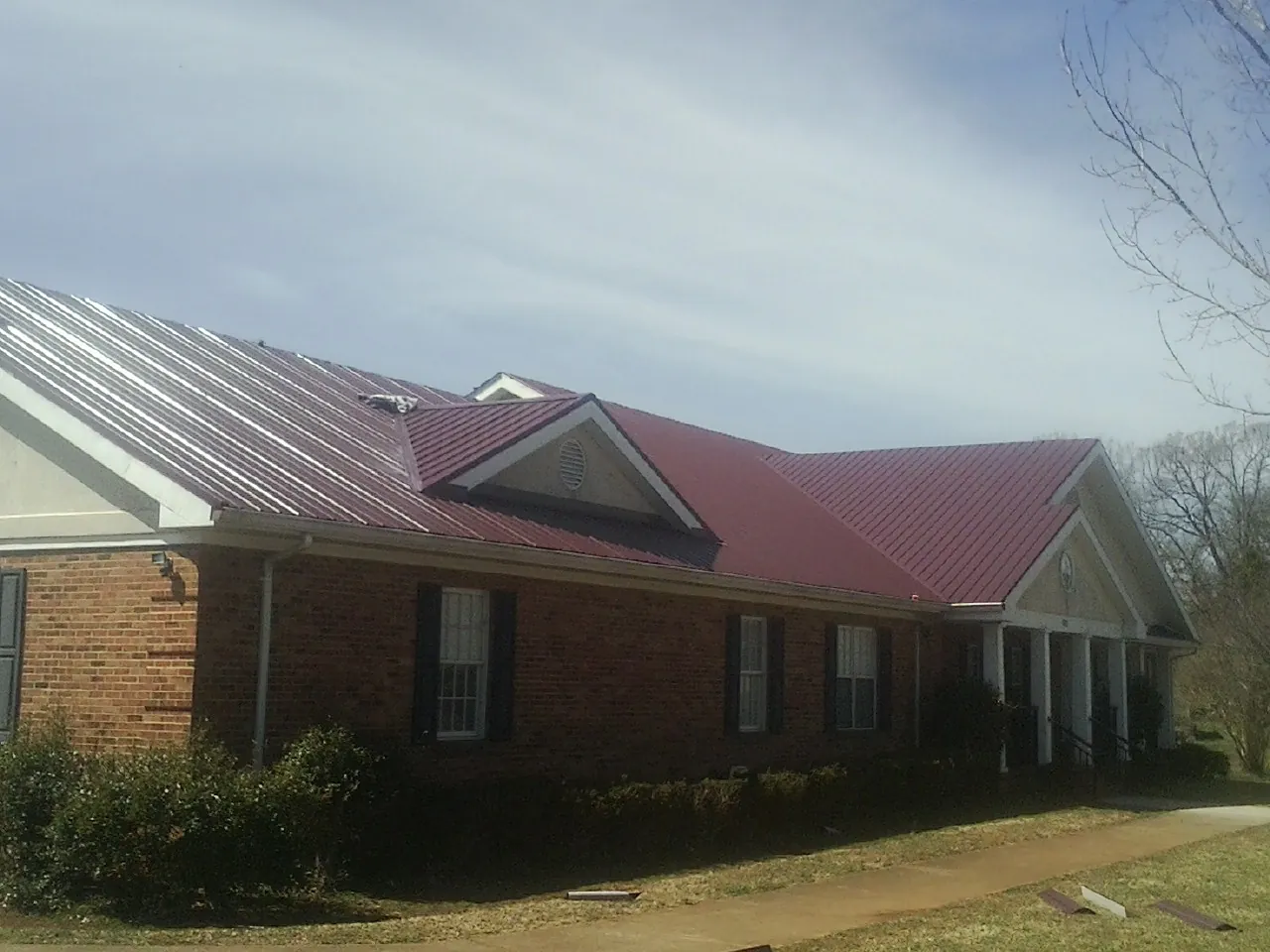 Red metal roof with gabled entries on a long brick building, from a Hail Damage Roof Repair job in Herscher