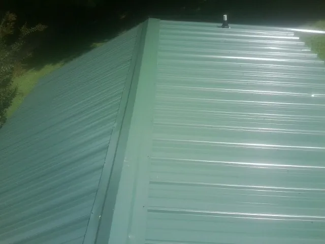 New green metal panels meeting at the ridge of a roof — Flat Roof Repair work by our crew in Herscher