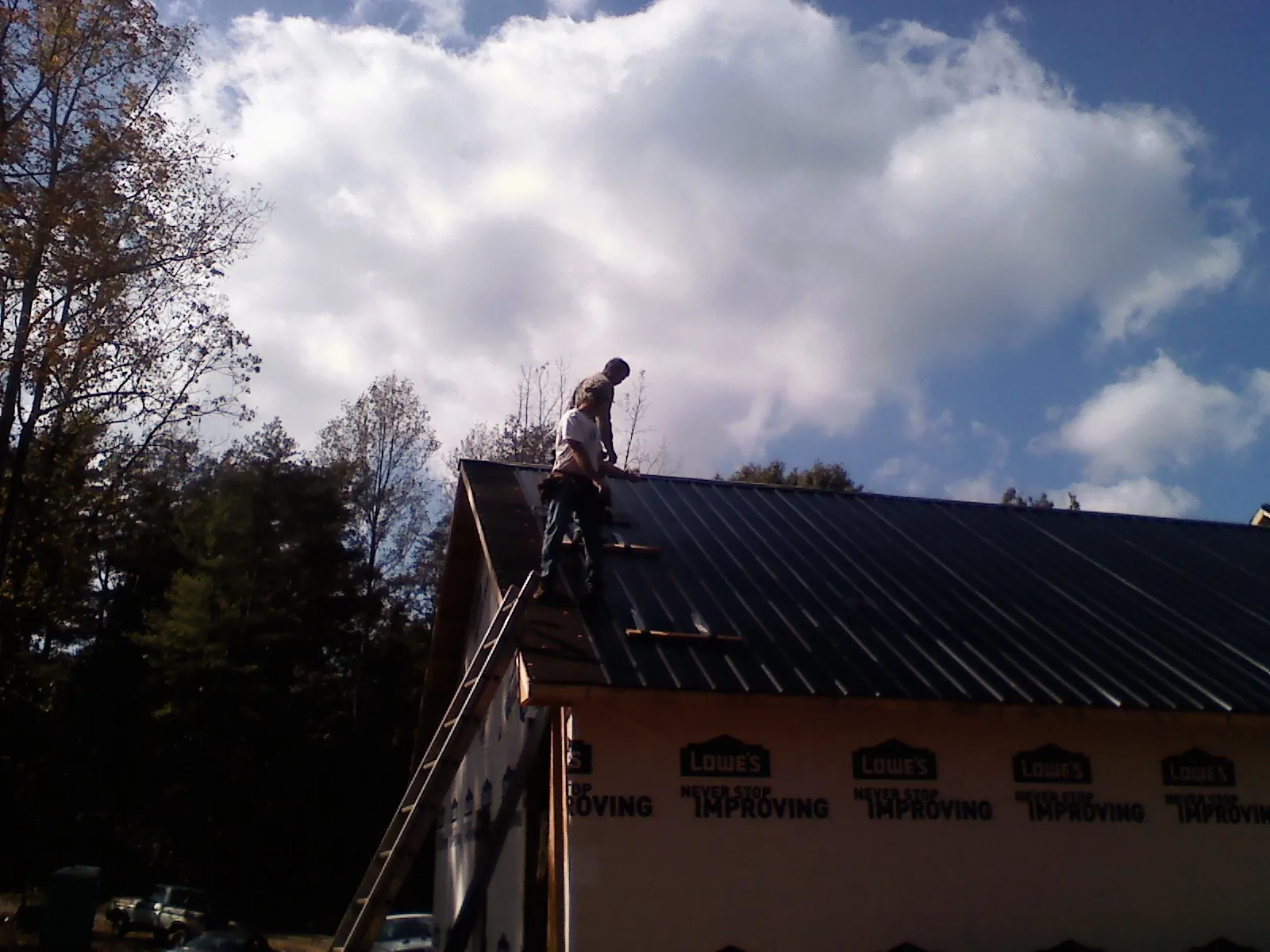 Roofer fastening dark metal panels high against a cloudy sky, from a Roof Inspection job in Herscher