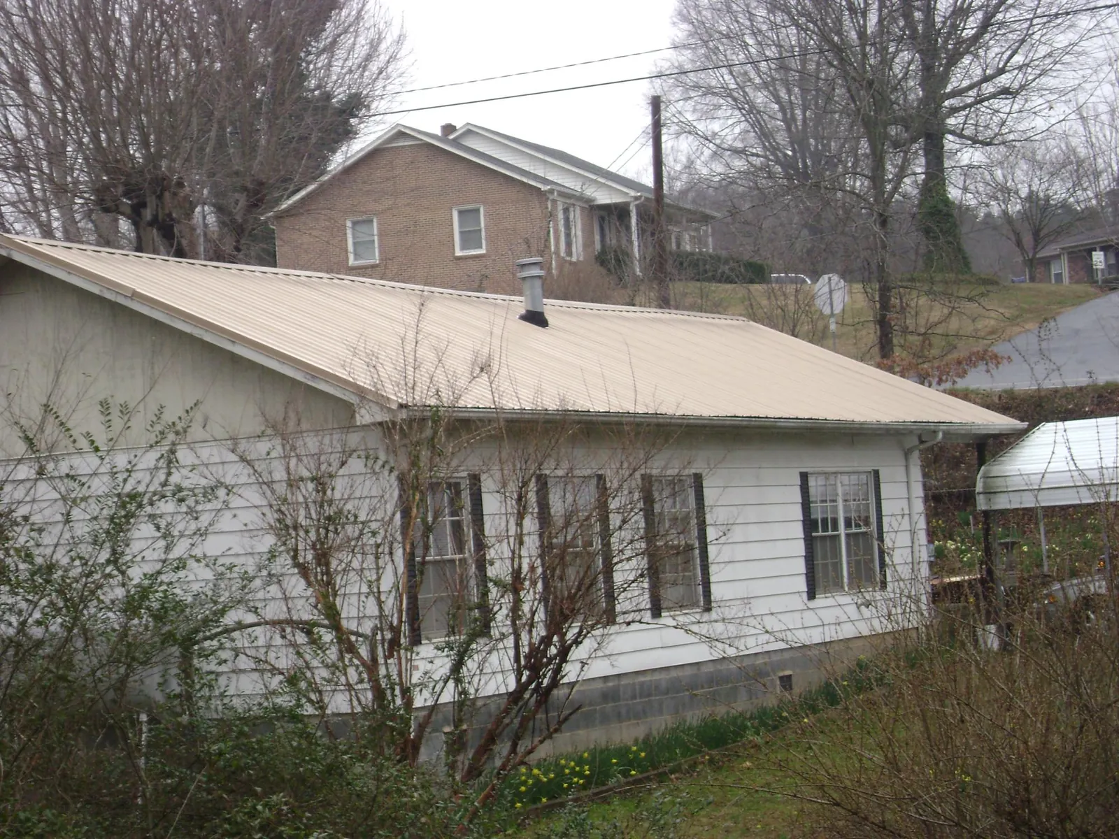 Tan metal roof on a white sided house set into a hillside — Commercial Roofing by Roofing Brothers in Herscher