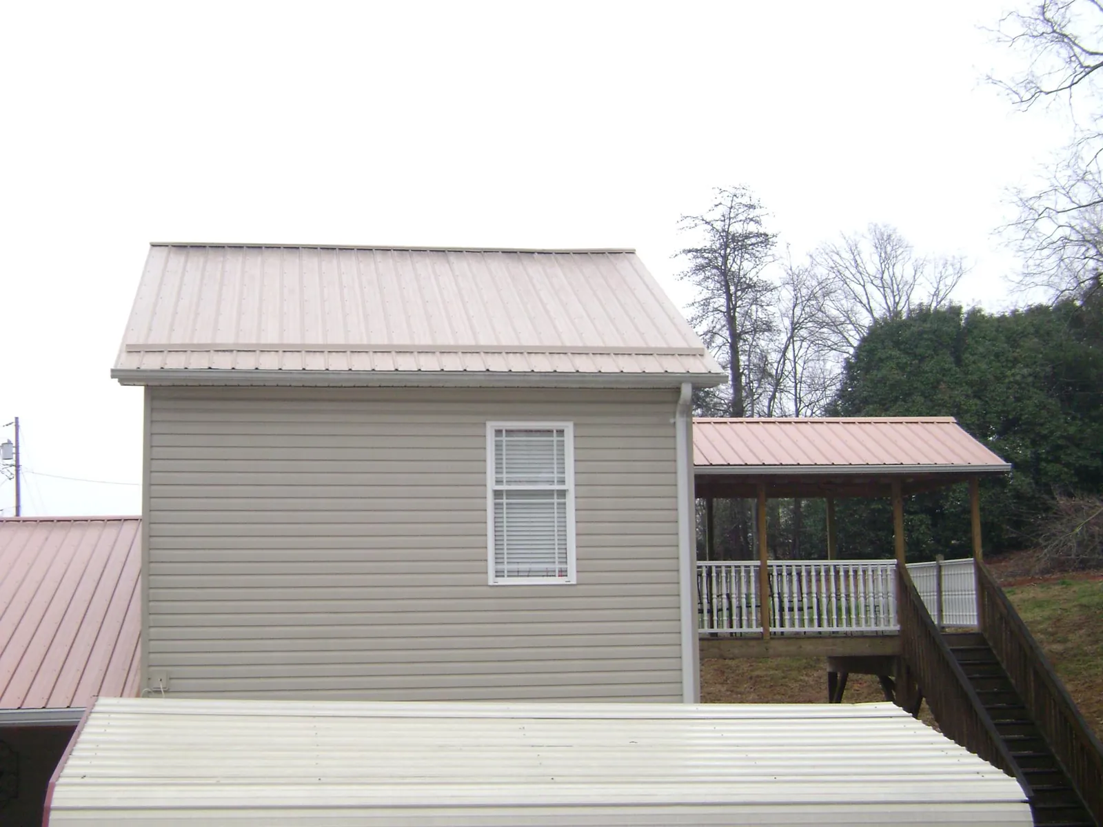 Tan metal roofs on a two story addition and attached porch, from a Roof Replacement job in Herscher