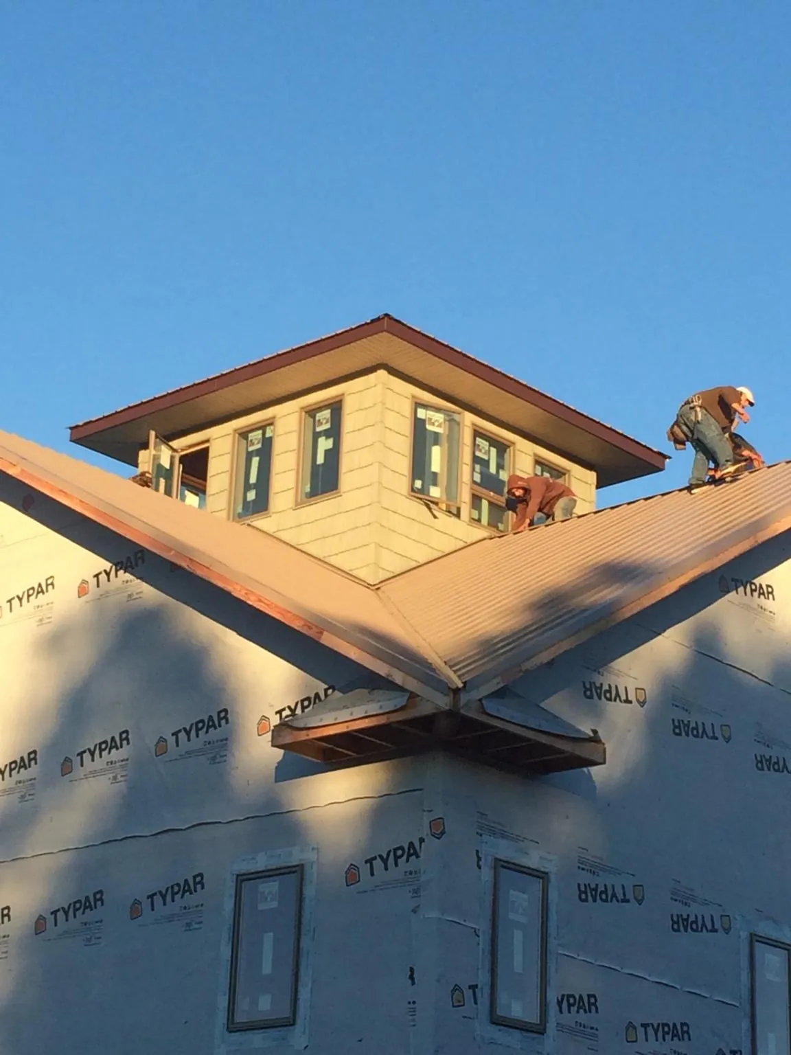 Roofers working around a rooftop cupola on a new metal roof at sunset — Roof Waterproofing in Herscher by Roofing Brothers